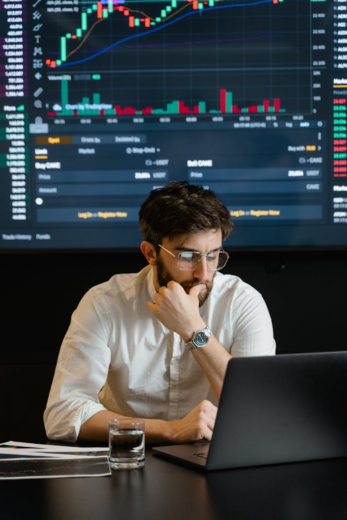gallery-05 Pensive businessman with a beard analyzing stock market trends on a laptop in an office setting.
